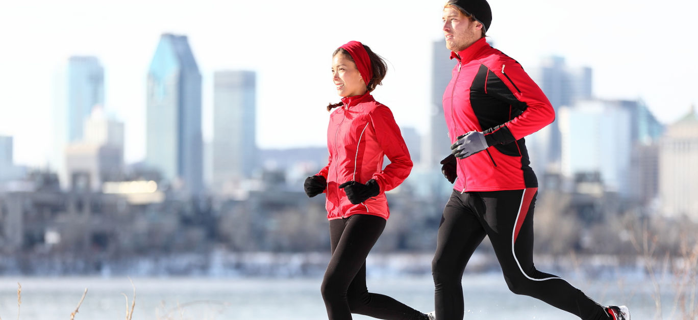 Runners running in winter snow with city skyline background
