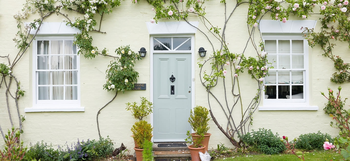 Home exterior UK. English house with green front door and wooden sash windows surrounded by climbing roses. England, UK