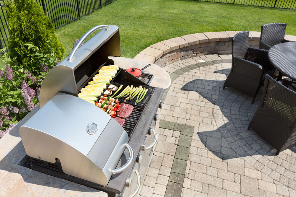 Grilling healthy food with corn kebabs meat and sausages on an outdoor gas barbecue on a luxury brick paved patio and summer kitchen in a neatly manicured back yard