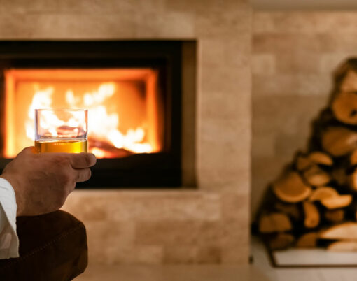 Man sitting at home by the fireplace and drinking a whiskey.