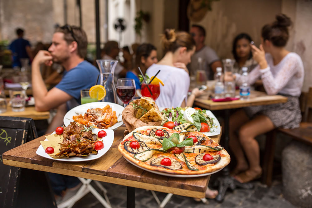 people eating traditional italian food in outdoor restaurant in Trastevere district in Rome, Italy.