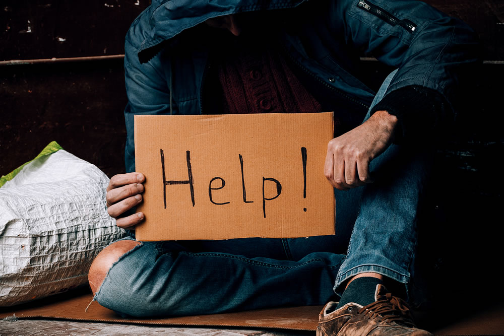 A homeless person holds a sign , asks for work, and seeks help