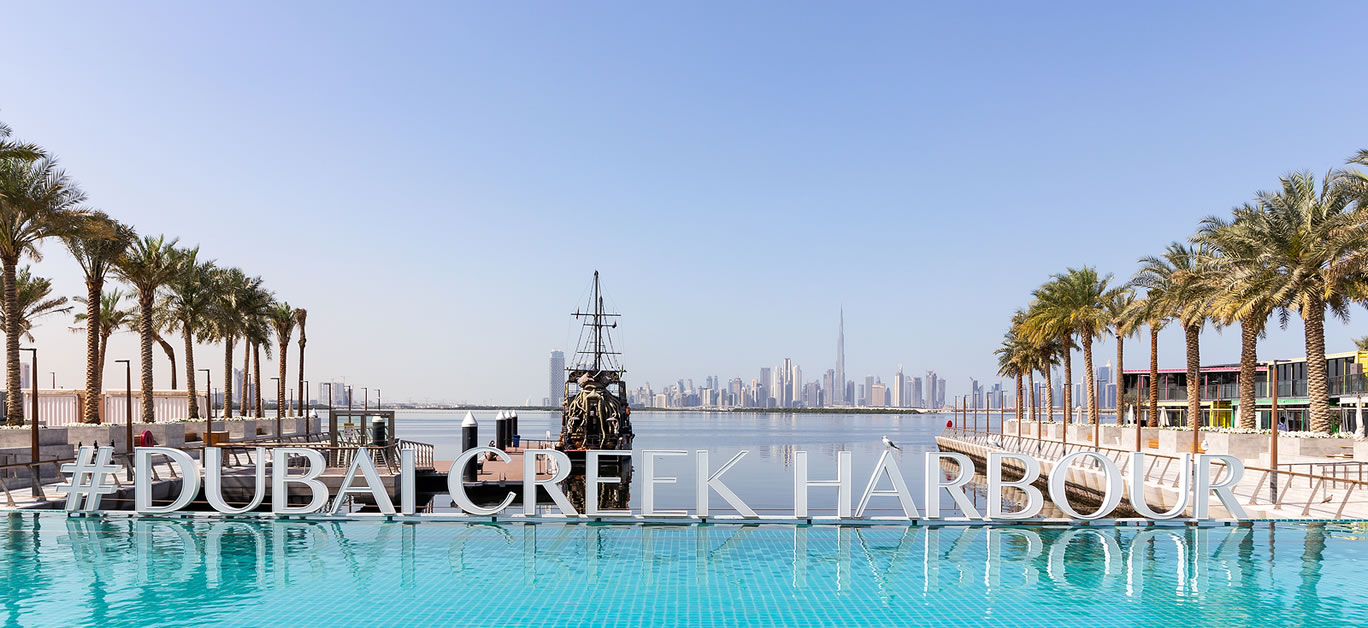 Dubai Creek Harbour sign by turquoise water pool with rows of palm trees
