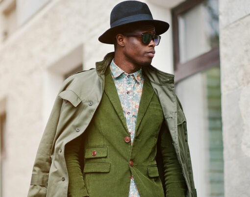Fashion portrait of black african american man on green velvet jacket black hat and coat cloak on his shoulders walking on streets of city background house with many windows