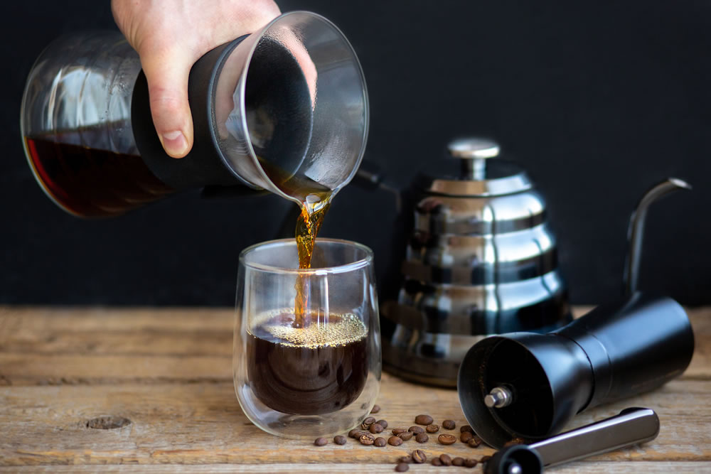 Hot coffee is pouring into a glass. Brewing coffee through a funnel
