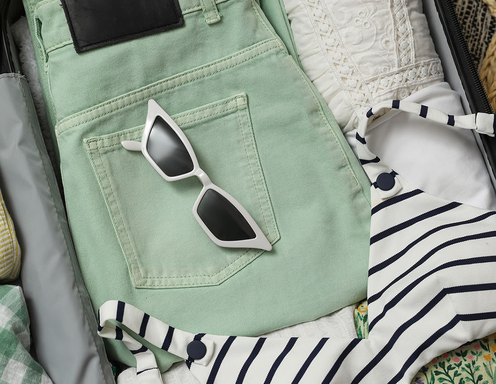 Open suitcase with summer clothes and sunglasses on floor, top view
