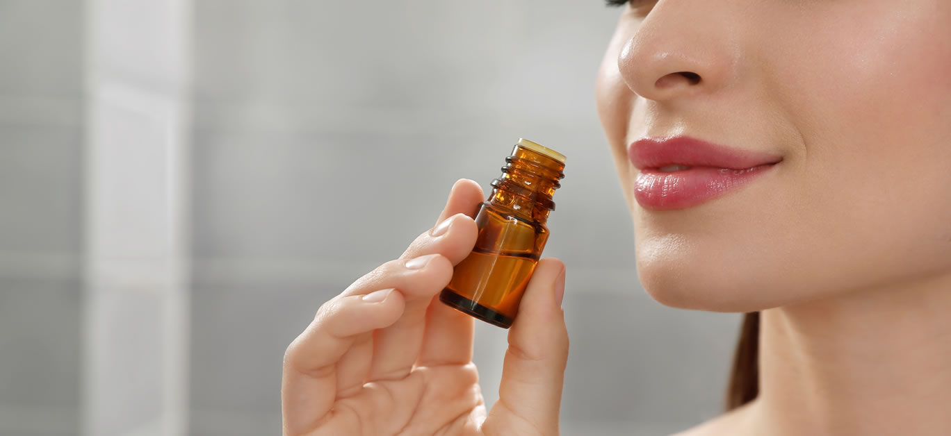 Young woman smelling essential oil indoors, closeup