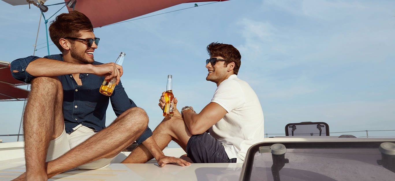 Joyful young male friends drinking beer on yacht in sea or ocean