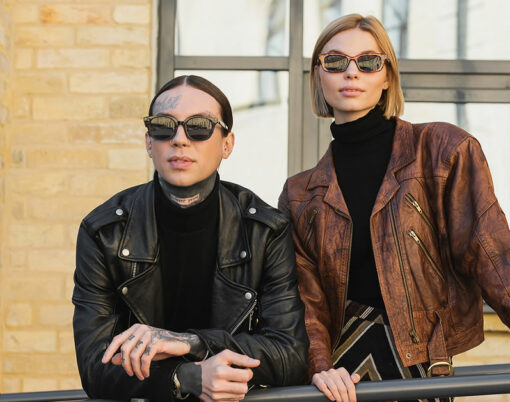 stylish couple in trendy sunglasses and leather jackets standing outdoors.
