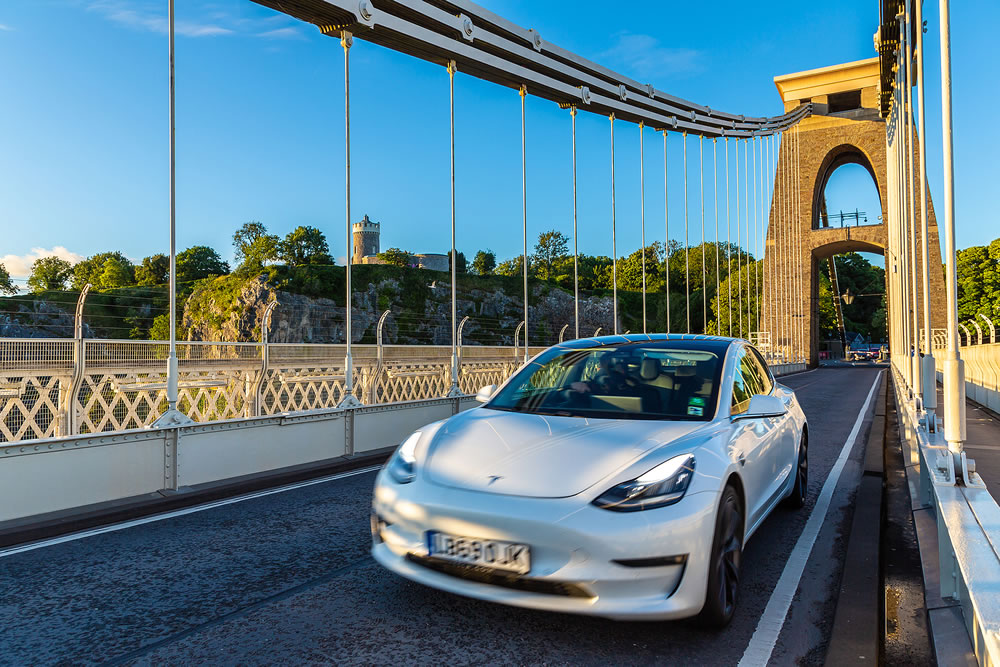 White electric Tesla car at Clifton Suspension Bridge in Bristol at sunset, UK