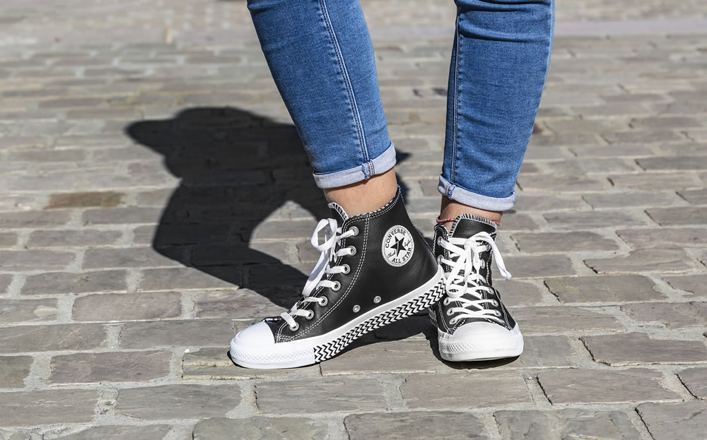 Image of the lower part of teenager\'s legs in jeans and All Star Converse sneakers in a cobblestone street.