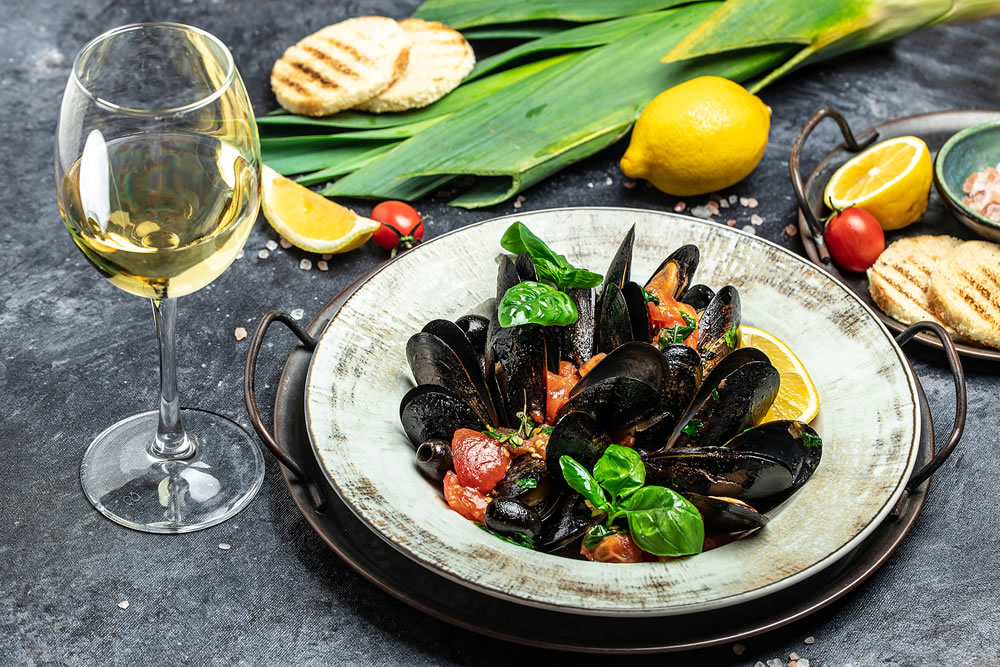 Fine dining in a seafood restaurant: a big dish of mussels with bottle of white wine with two wine glasses, on dark background