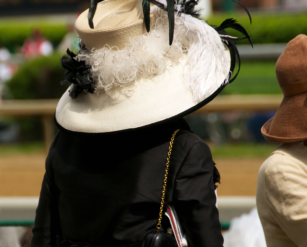 Woman watches the horse races in her high-fashion attire and accessories, including a very stylish black and white Derby hat.