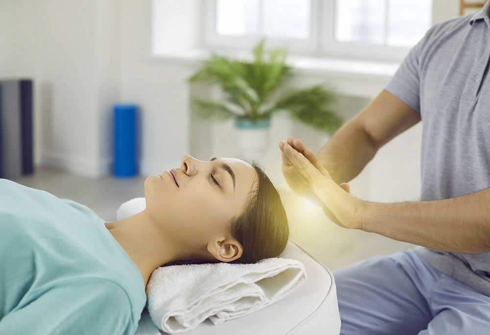 Woman relaxing and restoring energy during holistic healing session with Reiki therapist