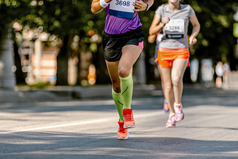 legs female runner athlete run marathon race on city street, legs woman jogger in compression socks