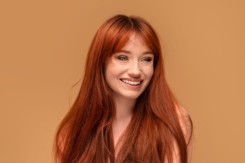 Authentic cheerful ginger girl with beautiful smile, natural freckles, long hair and fringe