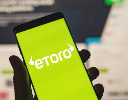 Man holding a smartphone with Etoro logo with blurred website as background. Trading platform, investing in stocks and cryptocurrencies