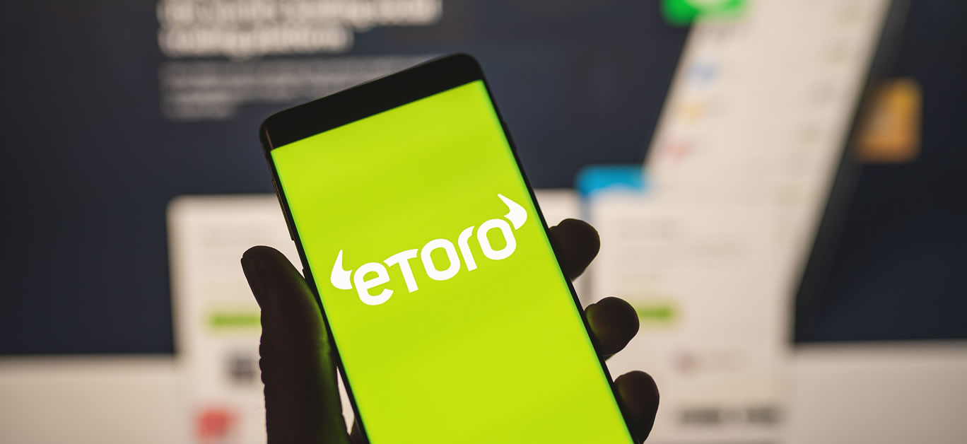 Man holding a smartphone with Etoro logo with blurred website as background. Trading platform, investing in stocks and cryptocurrencies
