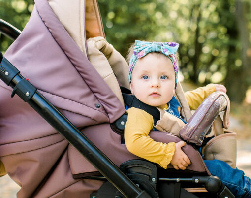 Cute little beautiful baby girl sitting in the pram or stroller and waiting for mom. Happy smiling child with blue eyes.