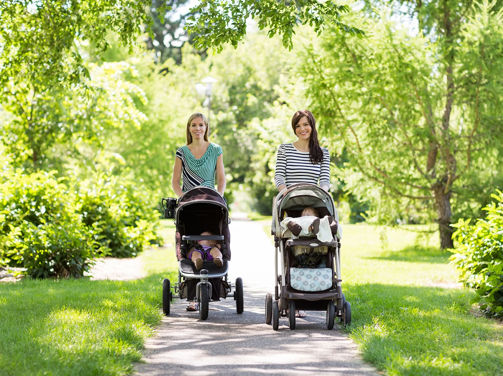 Portrait of happy mothers with their baby strollers walking together in park