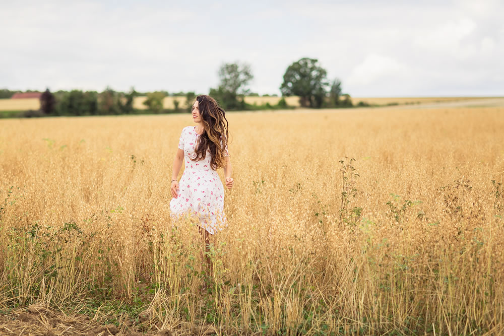 Young woman in white midi dress walking across the field with ripe golden ears of chickpeas