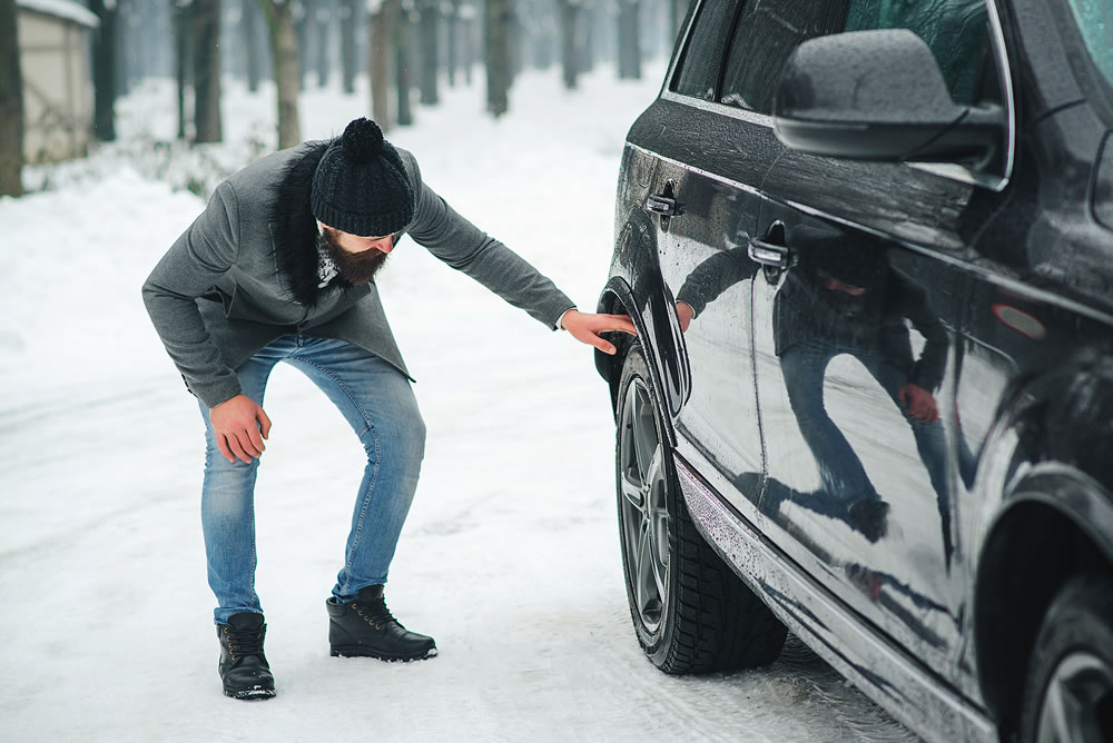 Man checking car tyre in winter. Businessman has problems with the wheels of the car. Winter snowy weather.