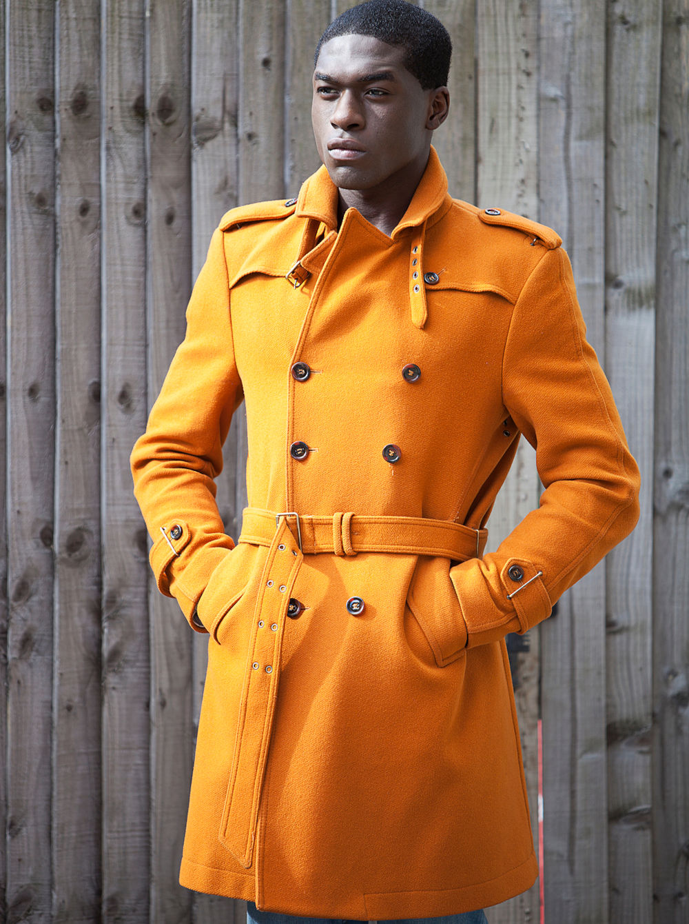 Young African American man in orange trench coat standing with hands in pockets