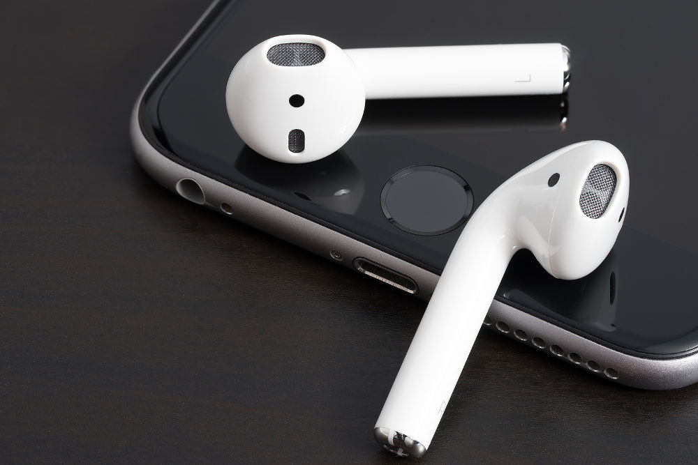 AirPods wireless headphones developed by Apple Inc. AirPods is on the open box and iphone.