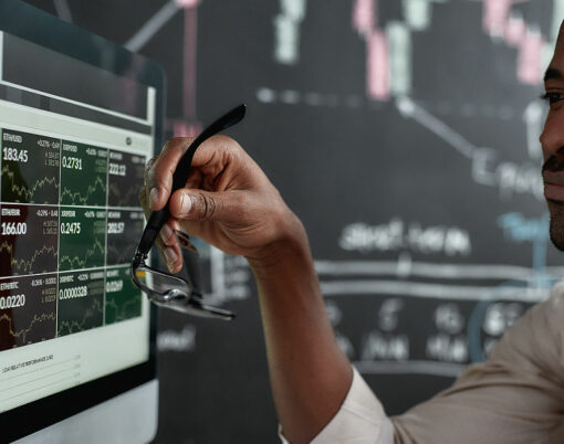 African businessman, trader sitting in front of computer screen and holding glasses while looking at graph chart.