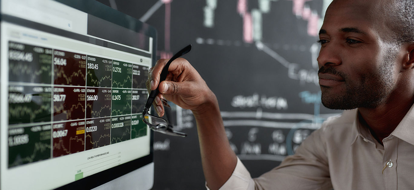 African businessman, trader sitting in front of computer screen and holding glasses while looking at graph chart.
