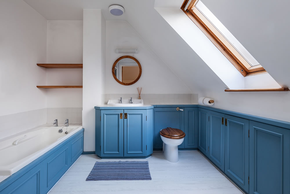 Attic style luxury attic style bathroom with blue painted cabinets, white walls, sloping ceiling and velux window