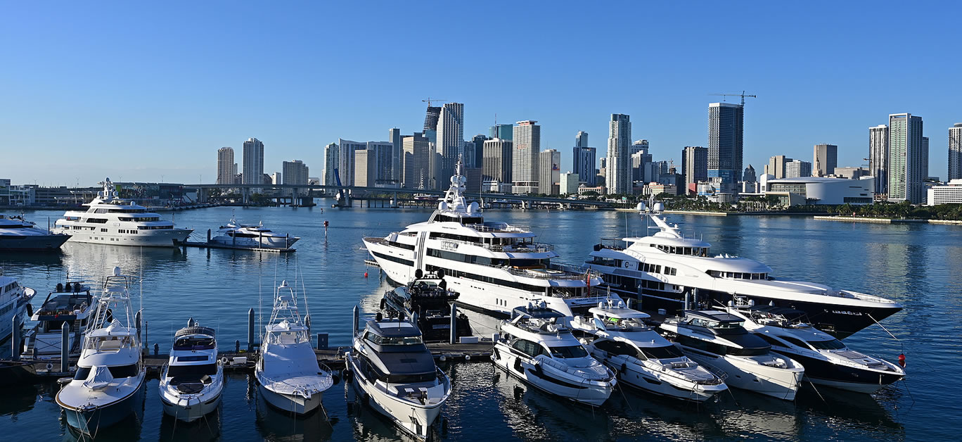 Super-yachts docked in Yacht Haven Grande Miami marina on clear calm morning with Miami skyline in background.