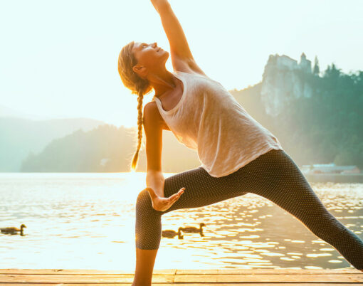 Beautiful woman practicing Yoga by the lake - Sun salutation series - Extended triangle pose - Water birds - Toned image