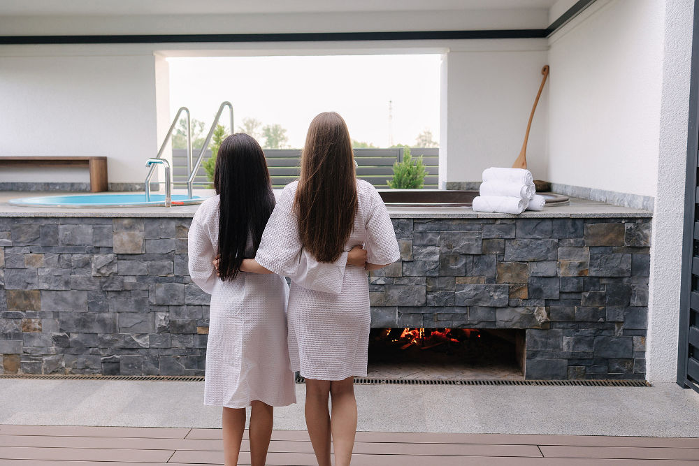 Back view of two pretty woman in white robe preparing for hot tube bathing. Relax outdoor in luxury resort