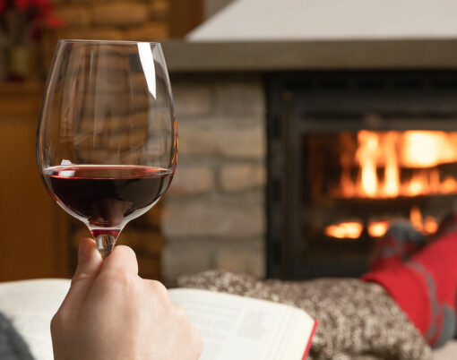 Beautiful women sitting in a cozy room by a warm fire place with a glass of wine and reading a book