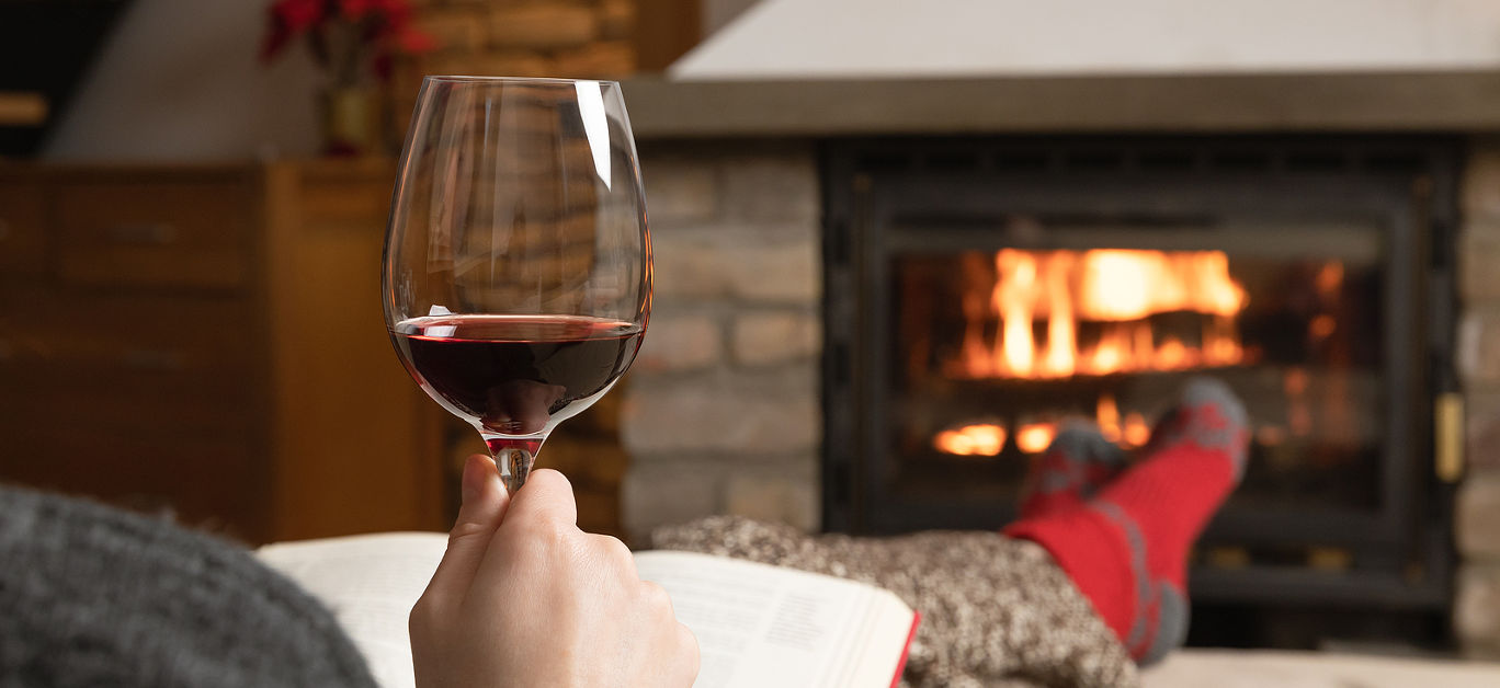 Beautiful women sitting in a cozy room by a warm fire place with a glass of wine and reading a book