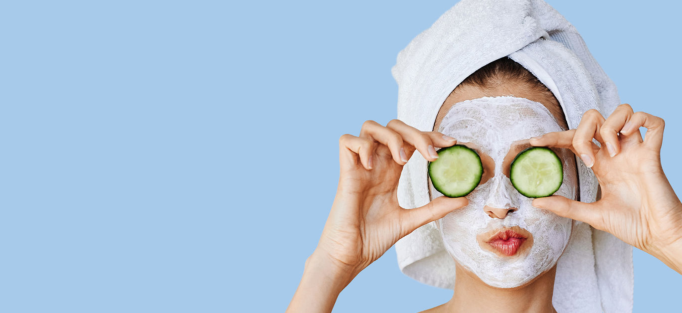 Beautiful young woman with facial mask on her face holding slices of fresh cucumber