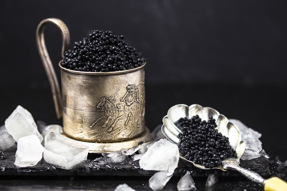 black caviar in a silver bowl with ice and a silver spoon on darck background. silver black caviar . black caviar