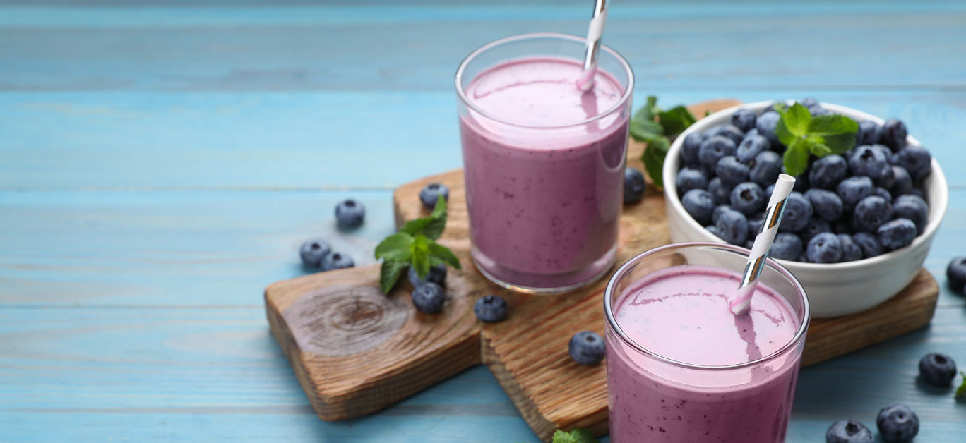 Glasses of blueberry smoothie with mint and fresh berries on turquoise wooden table.