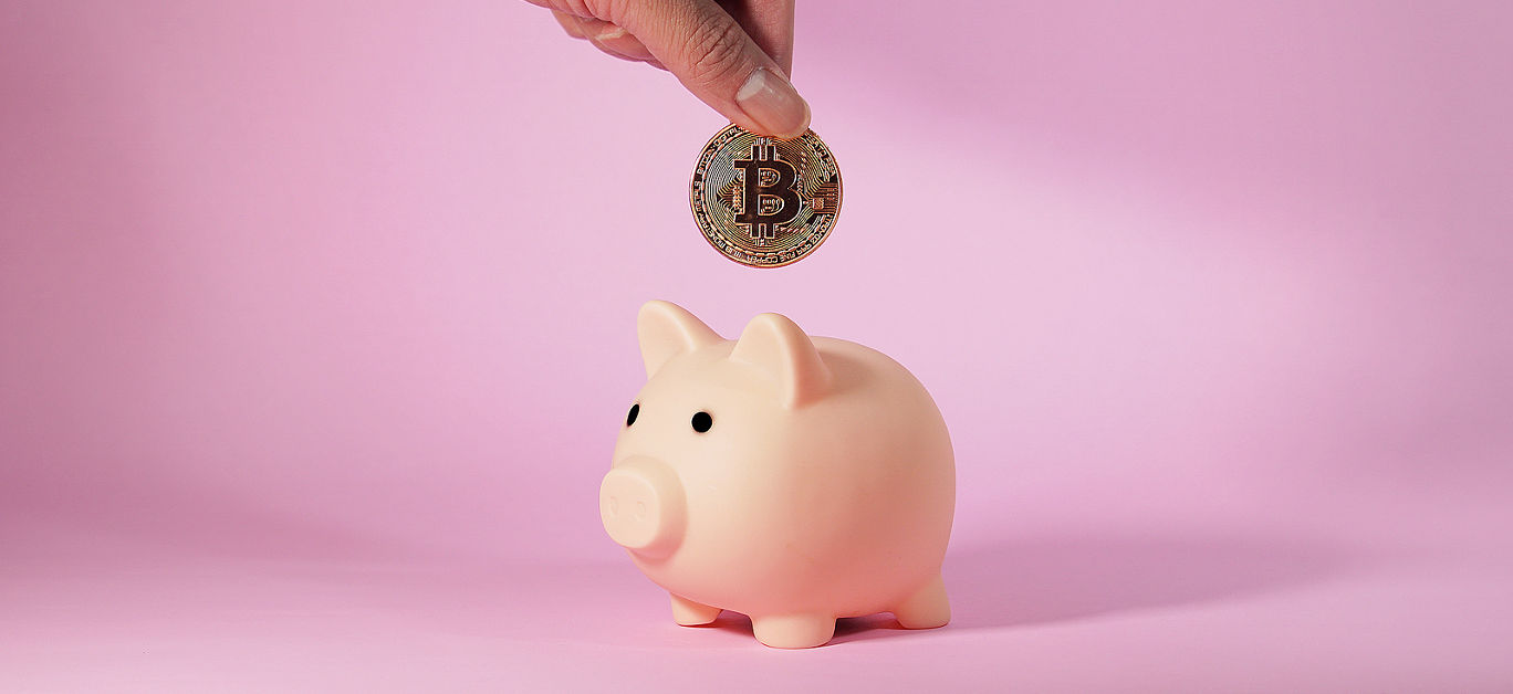 Hand of man drops metal bitcoin coin into piggy bank. Business and Finance.