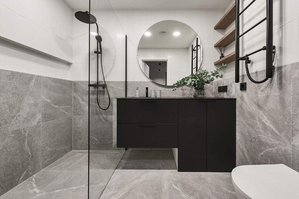 Modern minimalistic bathroom interior design with grey stone tiles, black furniture, eucalyptus in glass vase, round mirror