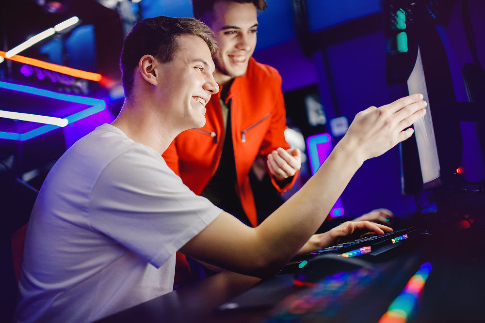 Team of two guys playing online video games analyzes strategy of fighting behind computer monitor in Internet cafe