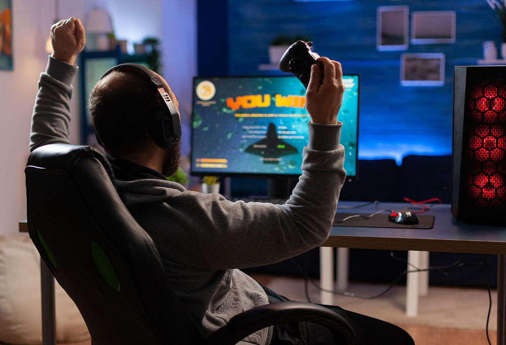 Winner gamer sitting on gaming chair at desk and playing space shooter video games with controller