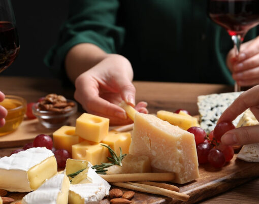Women with cheese plate and glasses of wine at wooden table, closeup