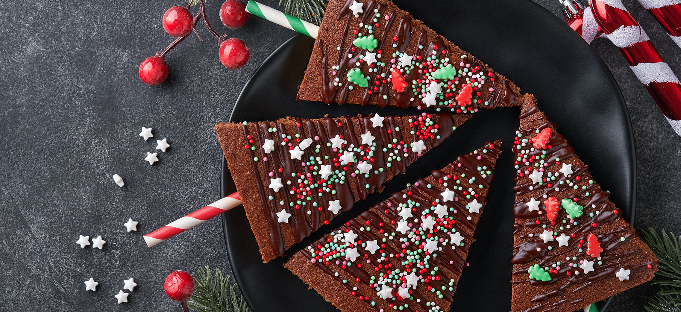 Chocolate brownies Christmas tree with chocolate icing and festive sprinkles on stone table