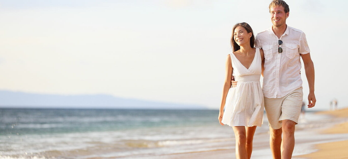 Couple walking on beach. Young happy interracial couple walking on beach smiling holding around each other. Asian woman, Caucasian man.