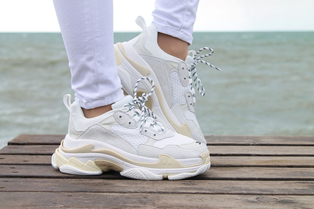 Female fashion sneakers. Close-up of woman feet wearing stylish sport or casual shoes. Girl walking near the beach