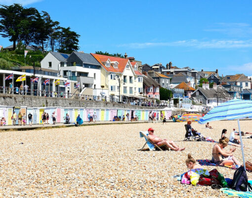 Holidaymakers relaxing on the pebble beach with the promenade and beach huts to the rear Lyme Regis