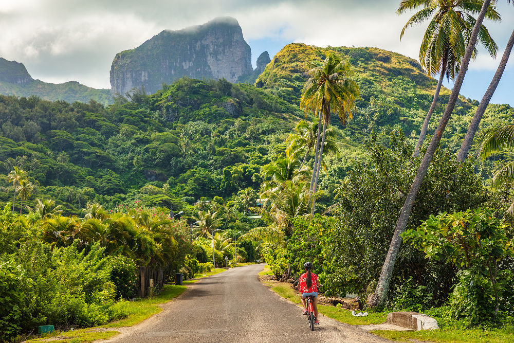 Biking tourist on summer vacation travel discovering by e-bike cycling through forest of Bora Bora island in Tahiti, French Polynesia.