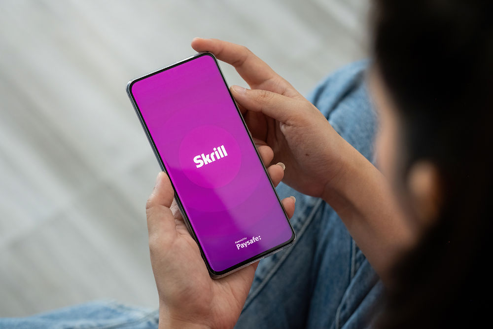 Skrill app. Woman using smartphone with skrill application. Brand logo photo.
